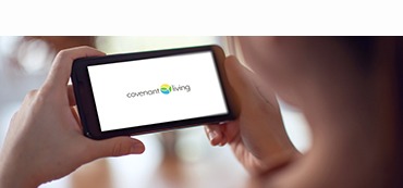 person holding a smartphone with the Covenant Living logo on the phone screen