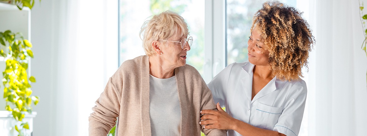 Caregiver assisting a smiling older women to walk with a walker