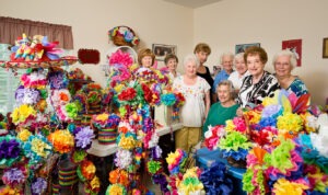 Group of women standing in craft room surrounded by colorful paper flowers