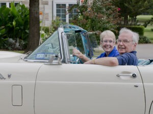Man driving tan convertible car with woman in passenger seat
