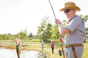 Man standing next to a pond holding his fishing rod with a fish hanging at the end