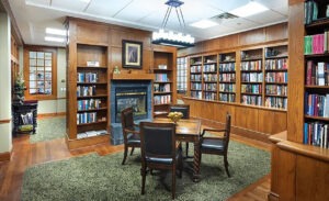 Library with shelves of books built into the walls and a table in front of a fireplace