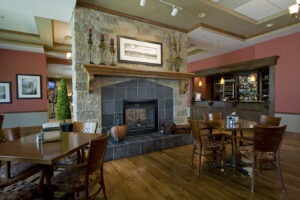 Bar at Inverness Village with tables and chairs in front of a large fireplace and bar counter in background