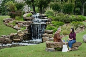 Two women eating lunch on stone bench in front of waterfall