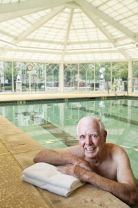Man hanging on edge of indoor pool smiling at camera