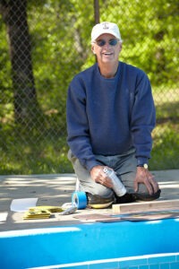 Man kneeling on ground spray painting interior of pool blue