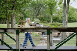 Woman in yellow sweater walking on wooden walking bridge in front of waterfall