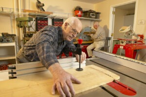 Inverness Village resident in woodworking shop with another resident sitting at saw behind