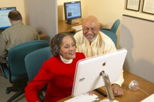 Man and woman sitting at desktop computer looking at screen and smiling