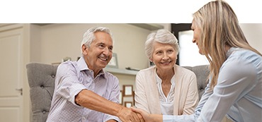 Older man and woman sitting at a table with a younger woman, the older man and younger woman shaking hands