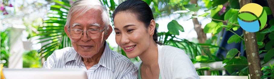 older man and his daughter sitting on a bench looking at a laptop